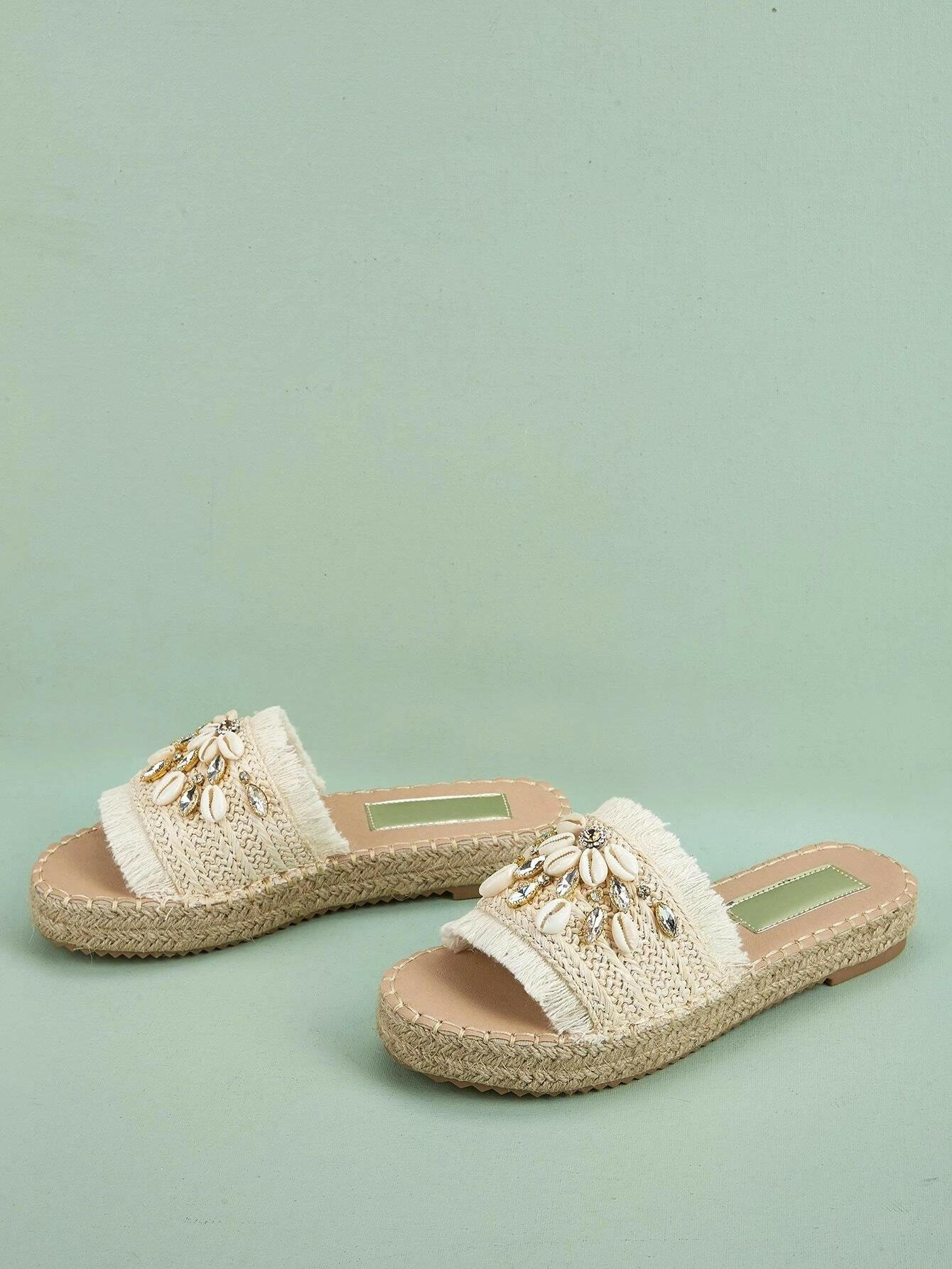 Espadrille sandals adorned with rhinestones and shell decorations. The rhinestones and shells add a touch of elegance and beachy charm to these stylish sandals. Perfect for adding a hint of sparkle and a coastal vibe to your summer outfits.
