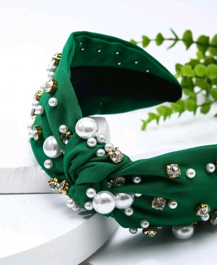 An olive green headband adorned with rhinestones and faux pearls, creating a chic and glamorous accessory. The headband is elegantly displayed, showcasing its intricate embellishments and stylish design.