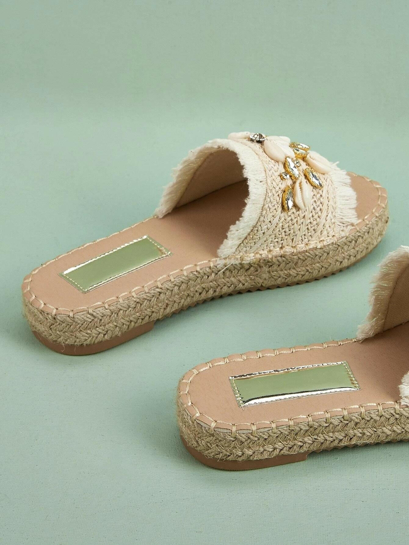 Espadrille sandals adorned with rhinestones and shell decorations. The rhinestones and shells add a touch of elegance and beachy charm to these stylish sandals. Perfect for adding a hint of sparkle and a coastal vibe to your summer outfits.