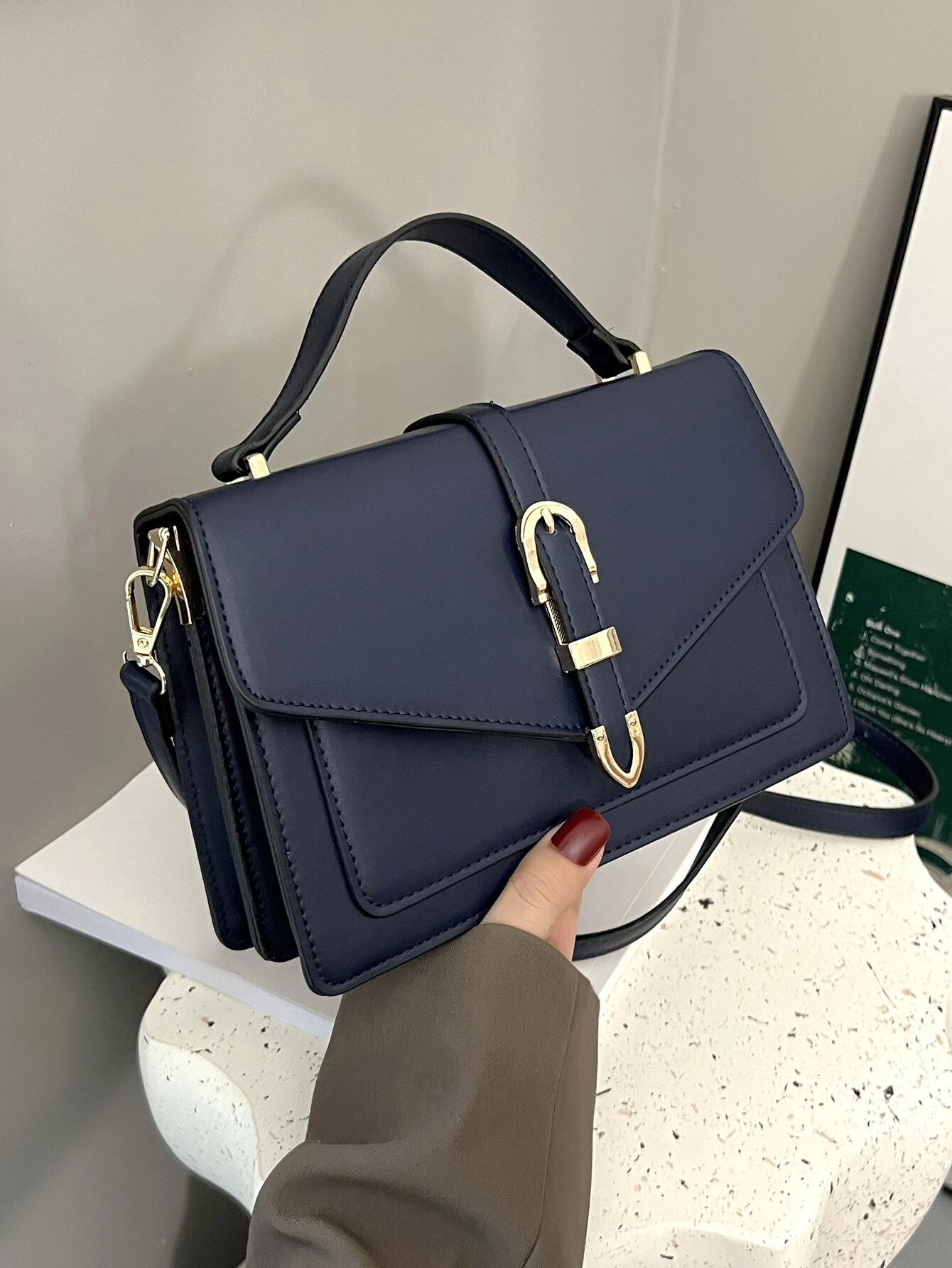 Minimalist navy blue square bag with metal decorative elements and flap closure. This accessory combines modern design with stylish embellishments, offering a chic and visually appealing way to carry your essentials.