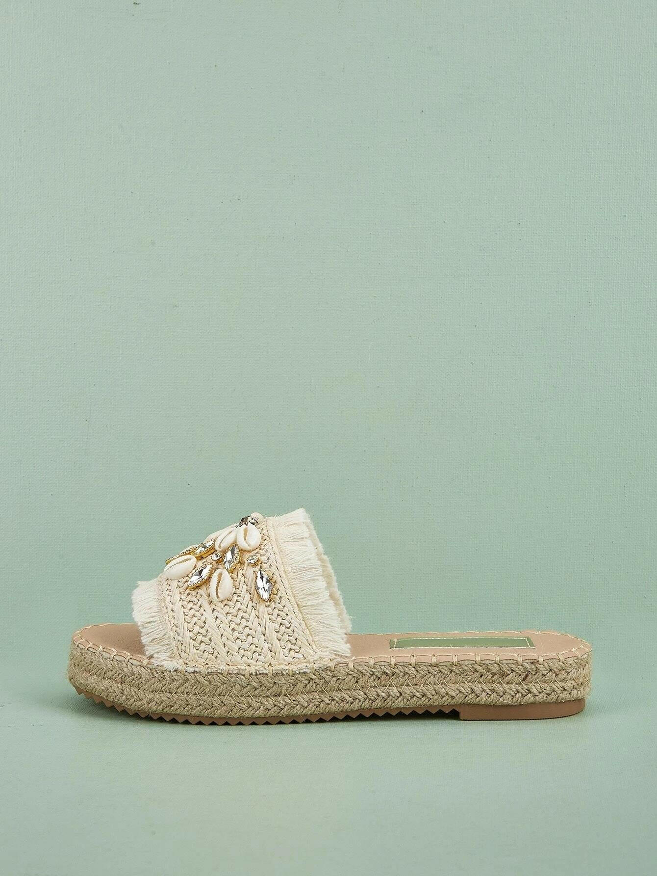 Espadrille sandals adorned with rhinestones and shell decorations. The rhinestones and shells add a touch of elegance and beachy charm to these stylish sandals. Perfect for adding a hint of sparkle and a coastal vibe to your summer outfits.