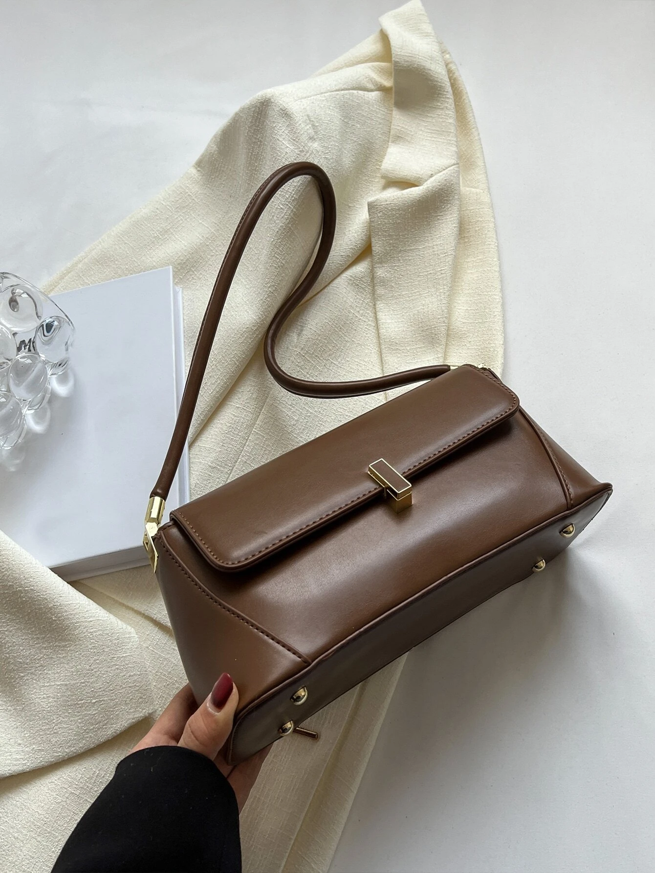Flap baguette bag adorned with metal decorative elements. This accessory blends modern design with stylish embellishments, offering a chic and eye-catching way to carry your essentials.