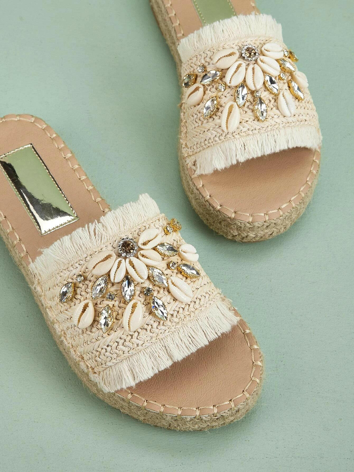 Espadrille sandals adorned with rhinestones and shell decorations. The rhinestones and shells add a touch of elegance and beachy charm to these stylish sandals. Perfect for adding a hint of sparkle and a coastal vibe to your summer outfits.
